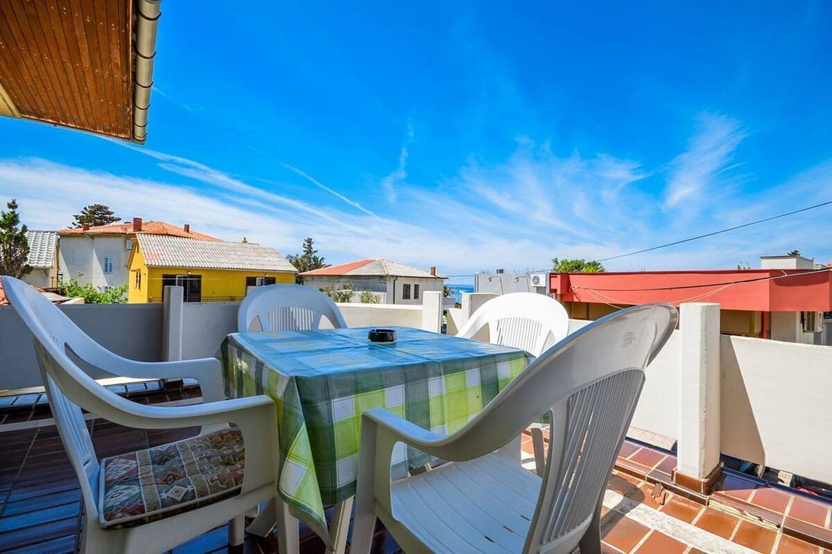 A terrace with a table and chairs, a view of neighboring houses, and a clear blue sky.