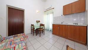 A compact kitchen with wooden cabinets, a dining table with chairs, and a bed with a colorful bedspread.