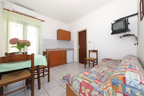 Una habitación compacta con cama, una mesa de comedor con sillas, una pequeña kitchenette y un televisor instalado en la pared.