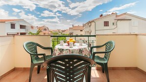A balcony with a table and chairs, a bowl of fruit, and a view of neighboring buildings.