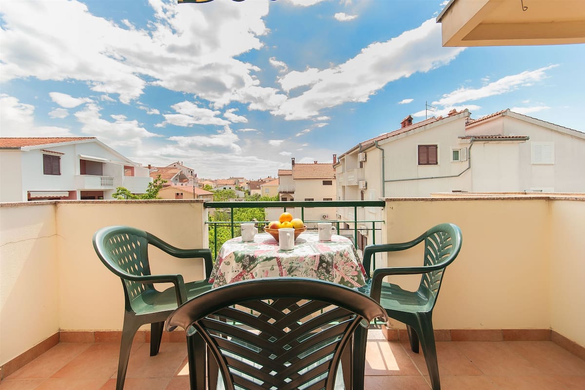 A balcony with a table and chairs, a bowl of fruit, and a view of neighboring buildings.