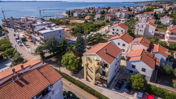 An aerial view of a coastal town with residential buildings, a marina, and a clear view of the sea.
