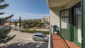 A balcony with a green chair, a car parked outside, and a view of a residential area with houses and a body of water.