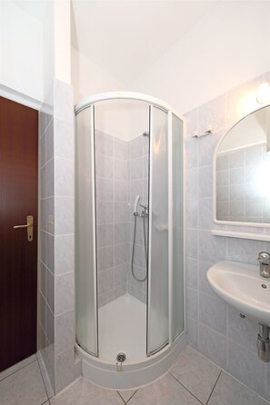 Ducha en esquina con puertas de vidrio, lavabo y espejo.
