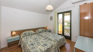 A bedroom with two beds, a wooden headboard, a nightstand with a lamp, a wooden wardrobe, and a window with a view.