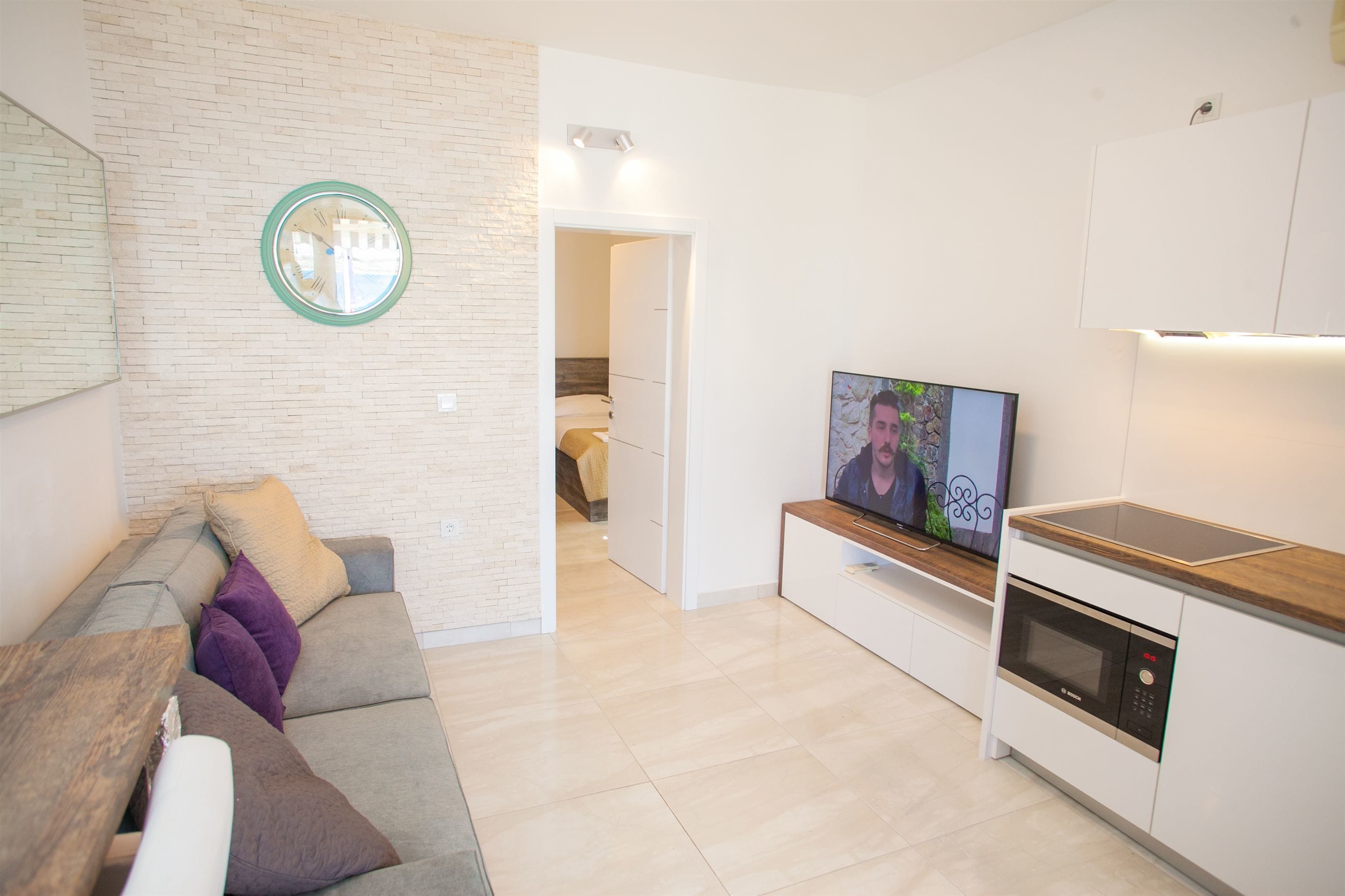 Ett modernt vardagsrum med en soffa, en tv och en köksdel med en mikrovågsugn.