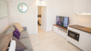 A modern living room with a sofa, a TV, and a kitchen area with a microwave. - Apartment Primorska (Novalja)