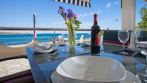A table set for dining with a view of the sea, a bottle of wine, and a vase with flowers. - Apartment Primorska (Novalja)