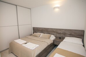 A bedroom with two beds, a wooden headboard, and a wall-mounted light fixture. - Apartment Primorska (Novalja)