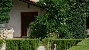 A house with a stone facade, a wooden door, and a well-maintained garden with hedges and flowering plants. - Apartments Vesna With Pool (Vodice)