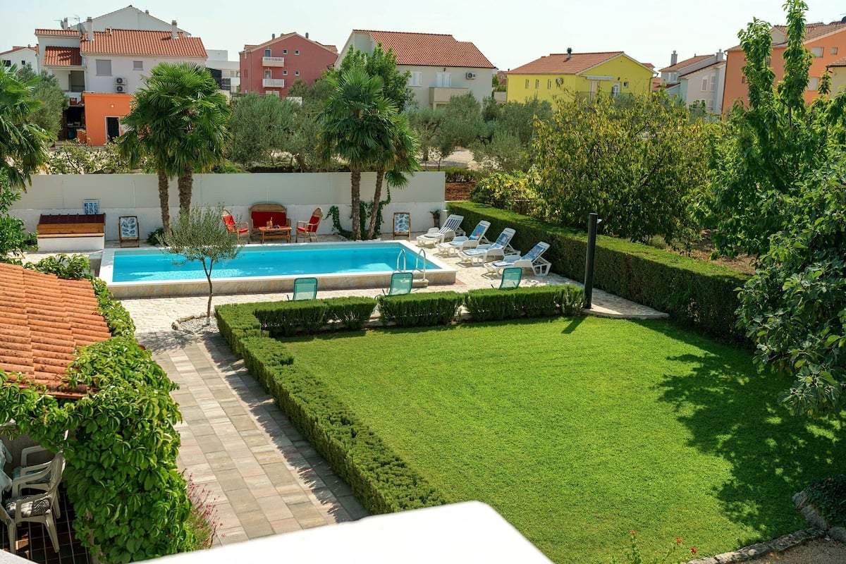 A swimming pool surrounded by neatly trimmed hedges and lounge chairs.