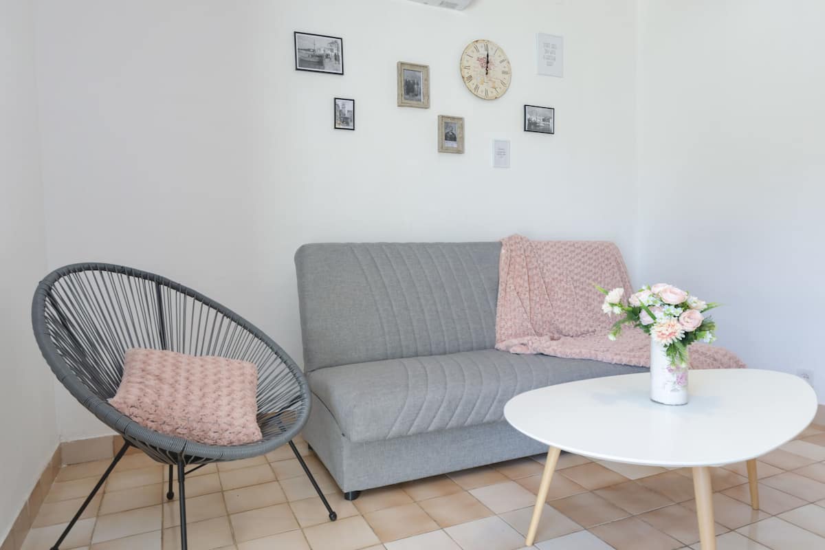A room with a grey sofa, a wicker chair, a white table, and a vase of flowers.