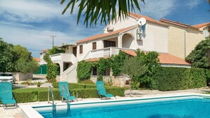 A swimming pool with a clear blue water, surrounded by a white pool deck and green lounge chairs. - Apartments Vesna With Pool (Vodice)