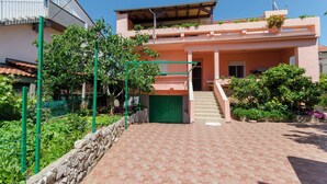 A two-story building with a green gate, a staircase leading to the upper floor, and a stone wall in the foreground. - Apartment Marija (Brodarica)