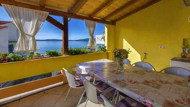 A covered outdoor dining area with a table and chairs, a yellow wall, and a view of the sea. - Apartment Marija (Brodarica)