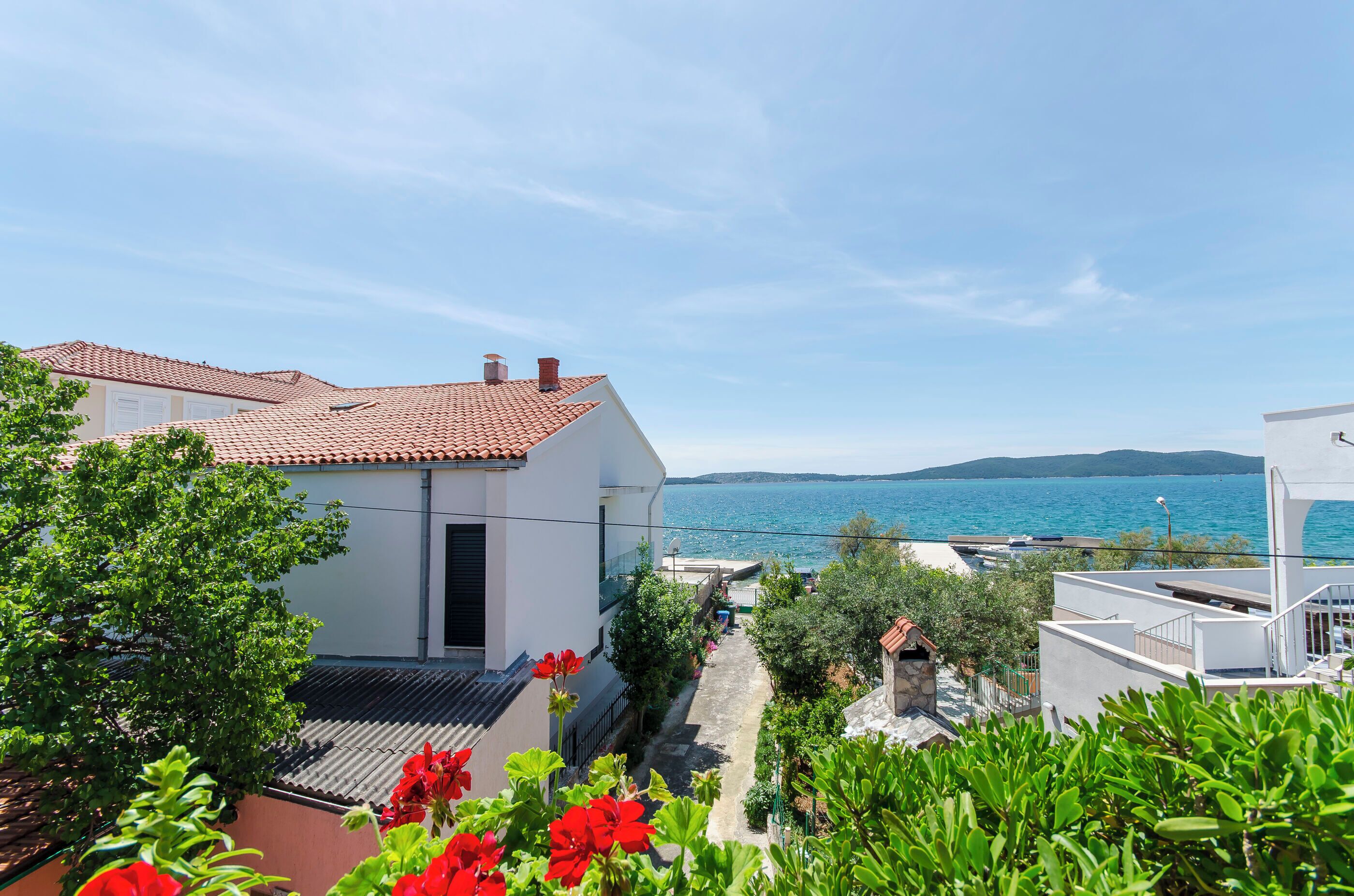 Ein Küstenwohngebiet mit terrakottafarbenen Dächern, einem schmalen Pfad und Blick auf das Meer.