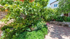 A garden with a stone wall, potted plants, and a brick pathway. - Apartment Marija (Brodarica)