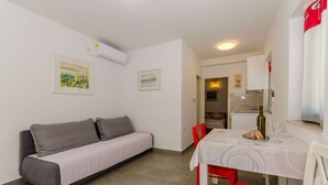 A compact living space with a grey sofa, a dining table with a white tablecloth, and red chairs. - Apartments Pharos (Stari Grad)