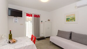 A room with a dining table, a sofa, a TV mounted on the wall, and a door with red curtains. - Apartments Pharos (Stari Grad)