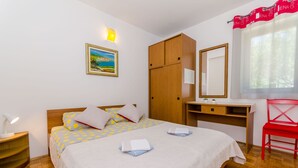 A bedroom with a bed, a desk, a chair, a wardrobe, a nightstand, and a painting on the wall. - Apartments Pharos (Stari Grad)