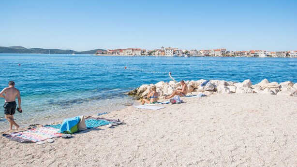 Una spiaggia con acque cristalline, un litorale roccioso e edifici sullo sfondo.