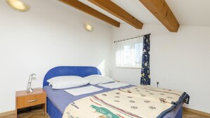 Camera da letto con un letto, un comodino, una lampada, una finestra con tende e una trave in legno al soffitto.