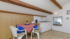 Una cucina con tavolo da pranzo apparecchiato per due persone, pensili in legno, una finestra con tenda e uno schienale piastrellato.