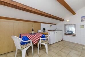 A kitchen with a dining table set for two, wooden cabinets, a window with a curtain, and a tiled backsplash.