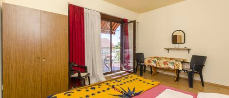 A room with a bed, a desk, a chair, a wardrobe, and a sliding glass door to the outside.