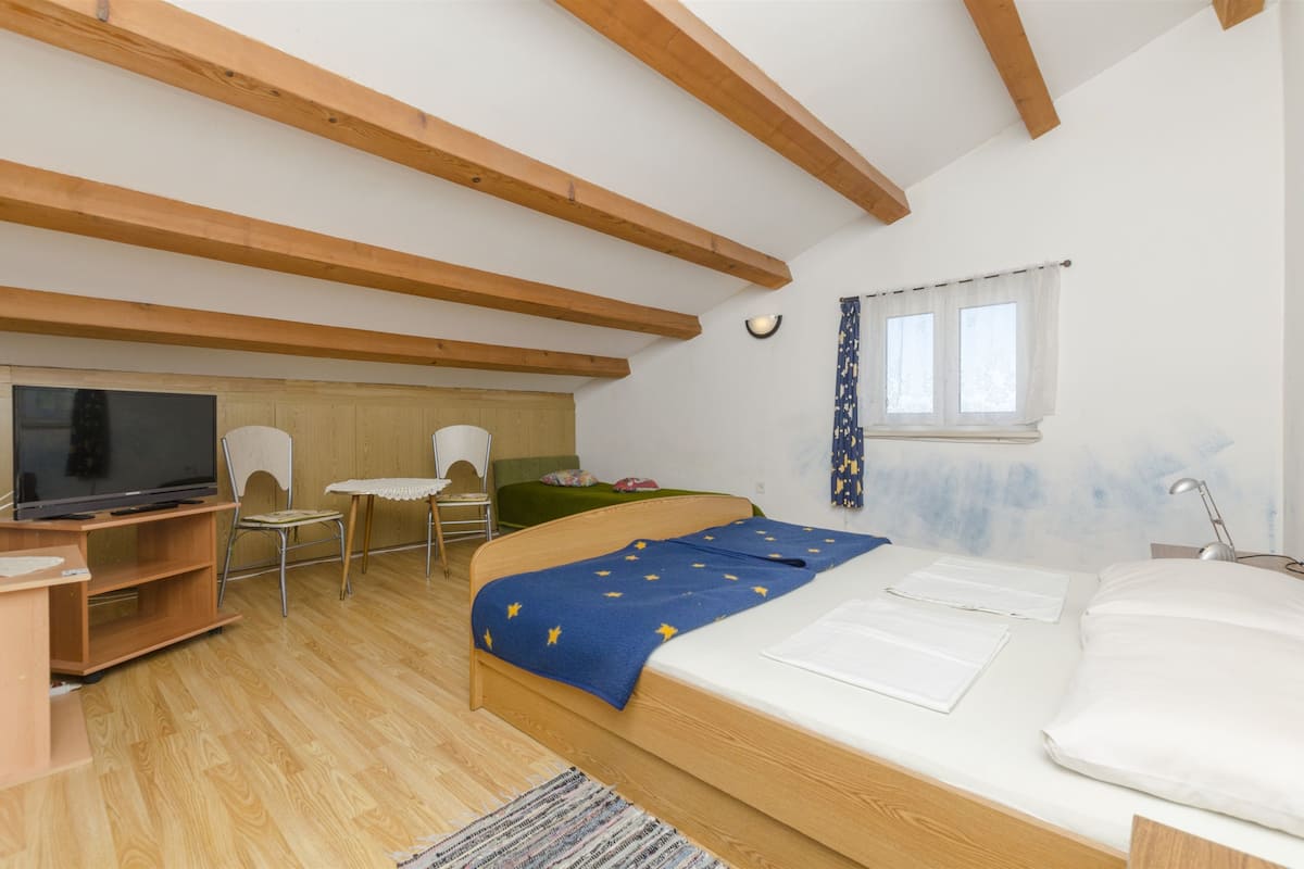 A bedroom with a bed, a desk, a chair, a television, and a window with curtains.
