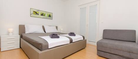 A bedroom with a bed, bedside tables, a sofa, a door, and a wall-mounted picture.