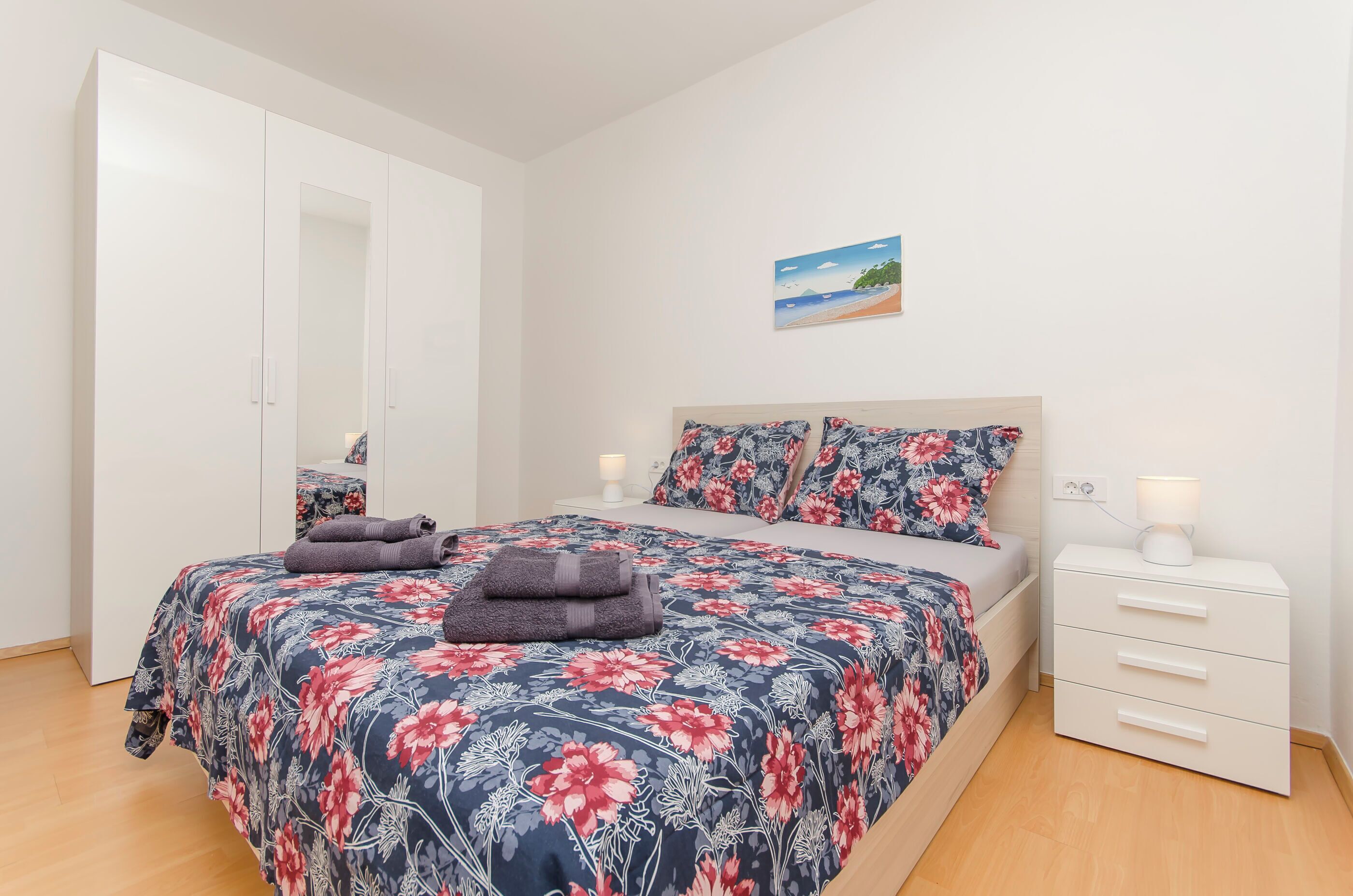 A bedroom with a bed, a nightstand, a wardrobe, and a wall-mounted picture.