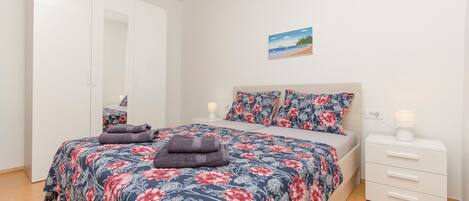 A bedroom with a bed, a nightstand, a wardrobe, and a wall-mounted picture.
