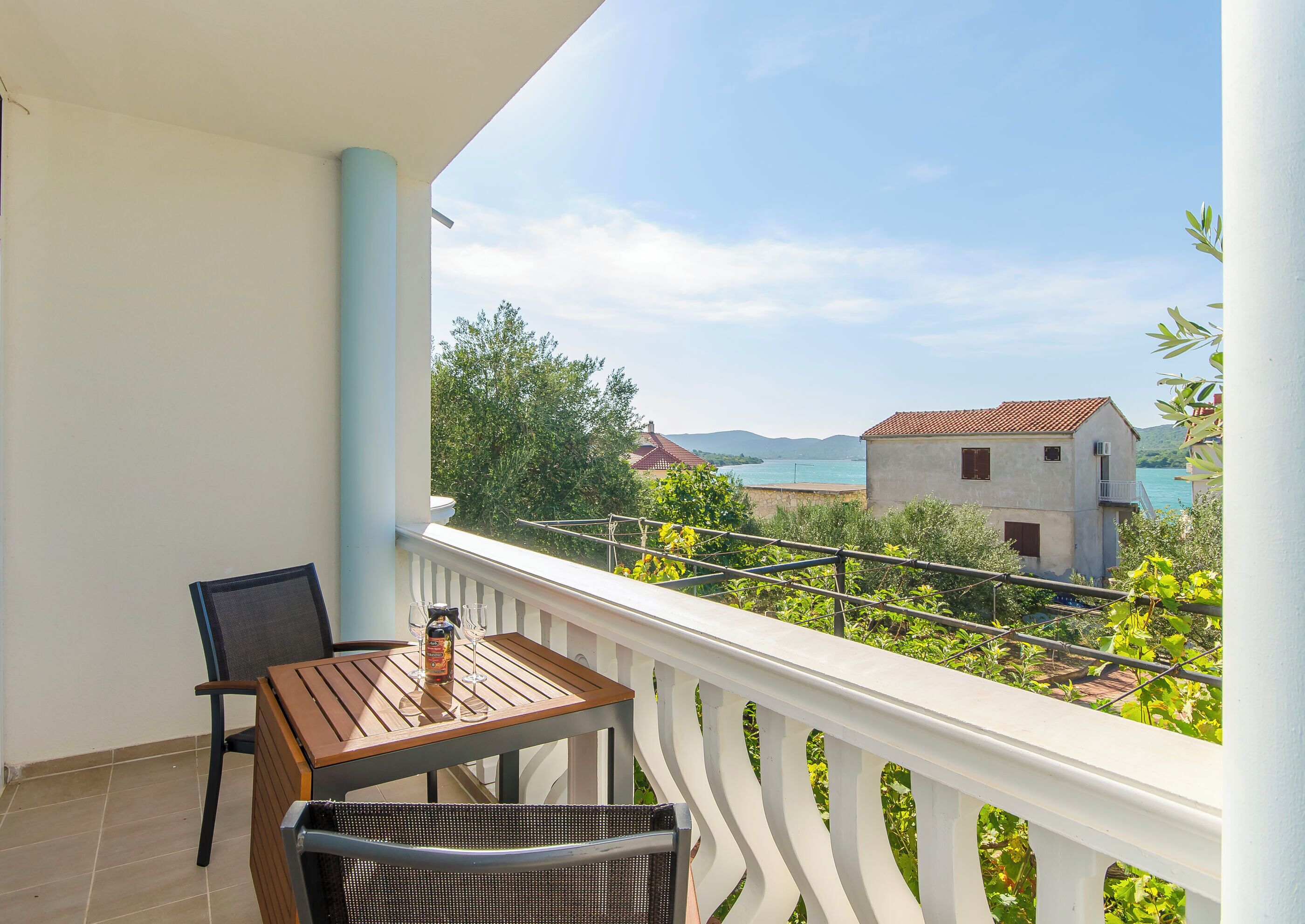 A balcony with a table and chairs, overlooking a coastal area with buildings and greenery.