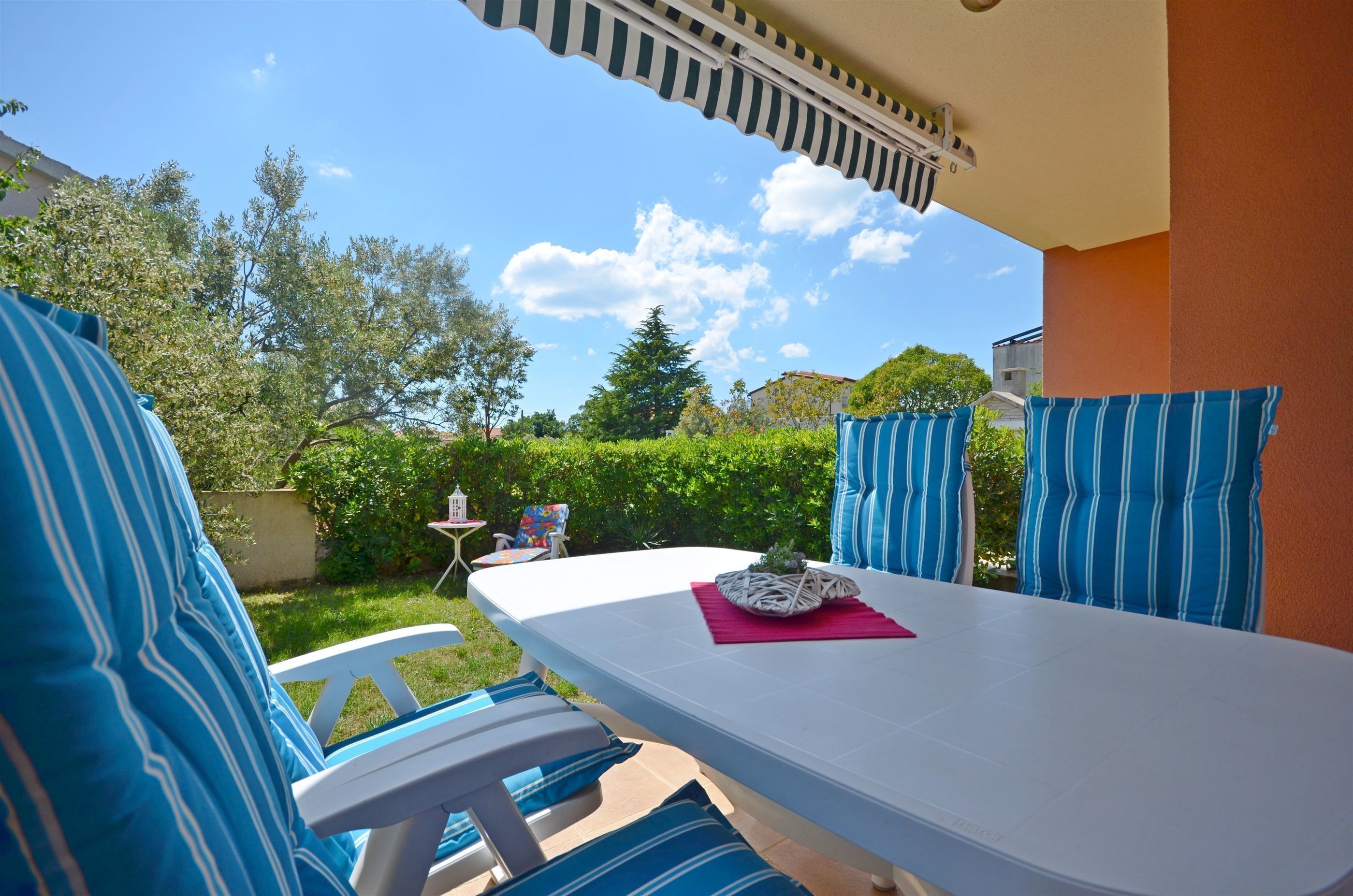 A patio with a white table, blue-striped cushions, and a small table with a plant.