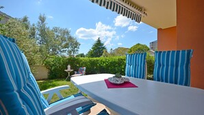 Un patio con una mesa blanca, cojines a rayas azules y una pequeña mesa con una planta.