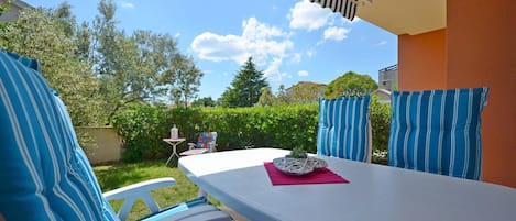 A patio with a white table, blue-striped cushions, and a small table with a plant.