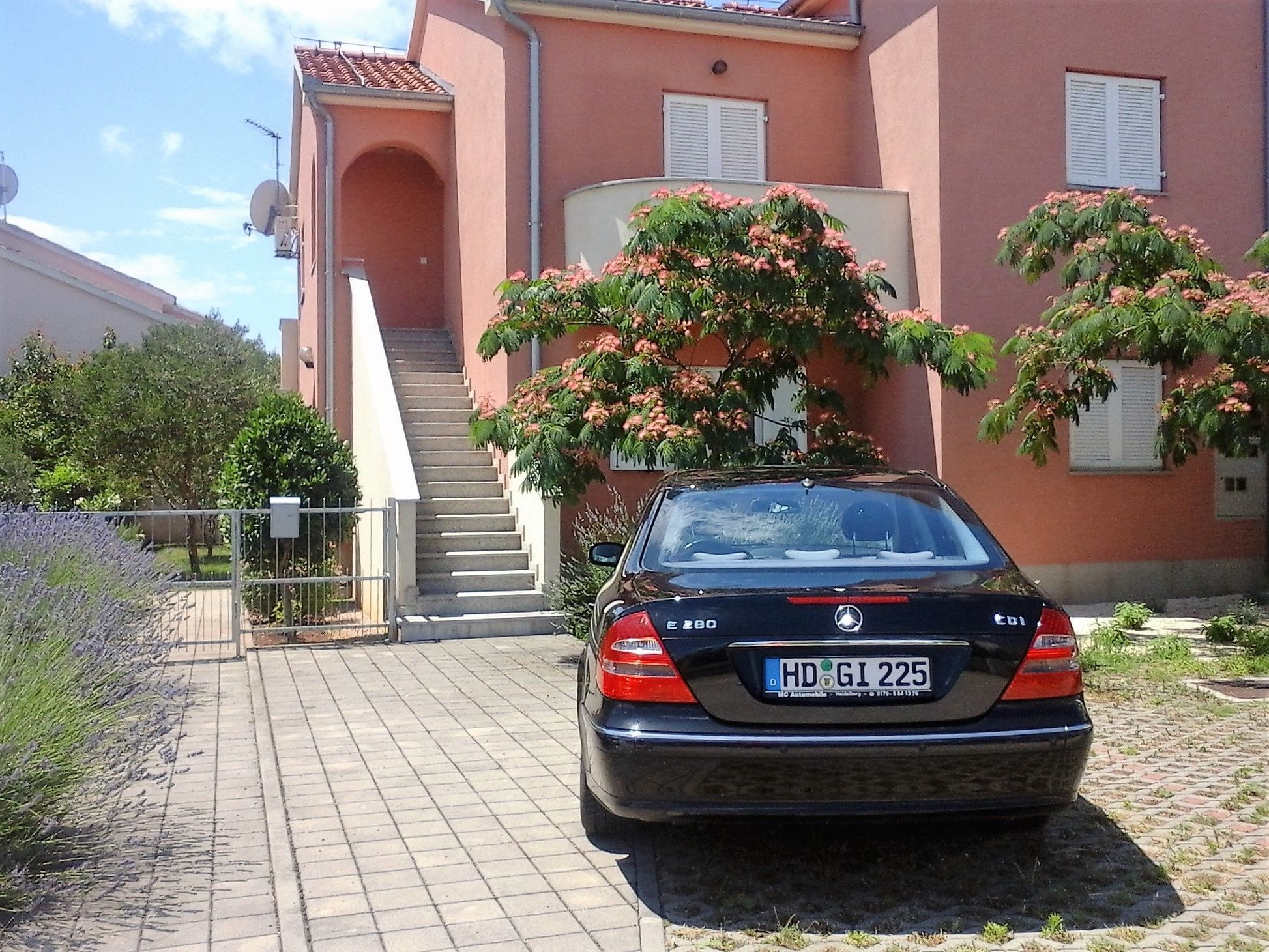 A black car parked in front of a pink building with a staircase leading to a door.