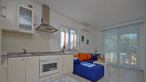 Una cocina moderna con armarios blancos, horno integrado y una zona de comedor con sofá azul y cojines naranjas.