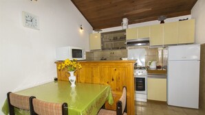 Una piccola cucina con mobili in legno, un forno a microonde, un fornello e un frigorifero. C'è un tavolo da pranzo con sedie e un vaso con fiori.