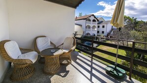 Un balcone con mobili in vimini e un tavolo, con vista su un edificio e un paesaggio verde.