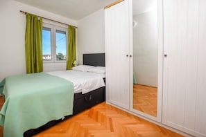 A bedroom with a bed, a wardrobe, a window with curtains, and a lamp. - Apartments Ercegovic (Rogoznica)