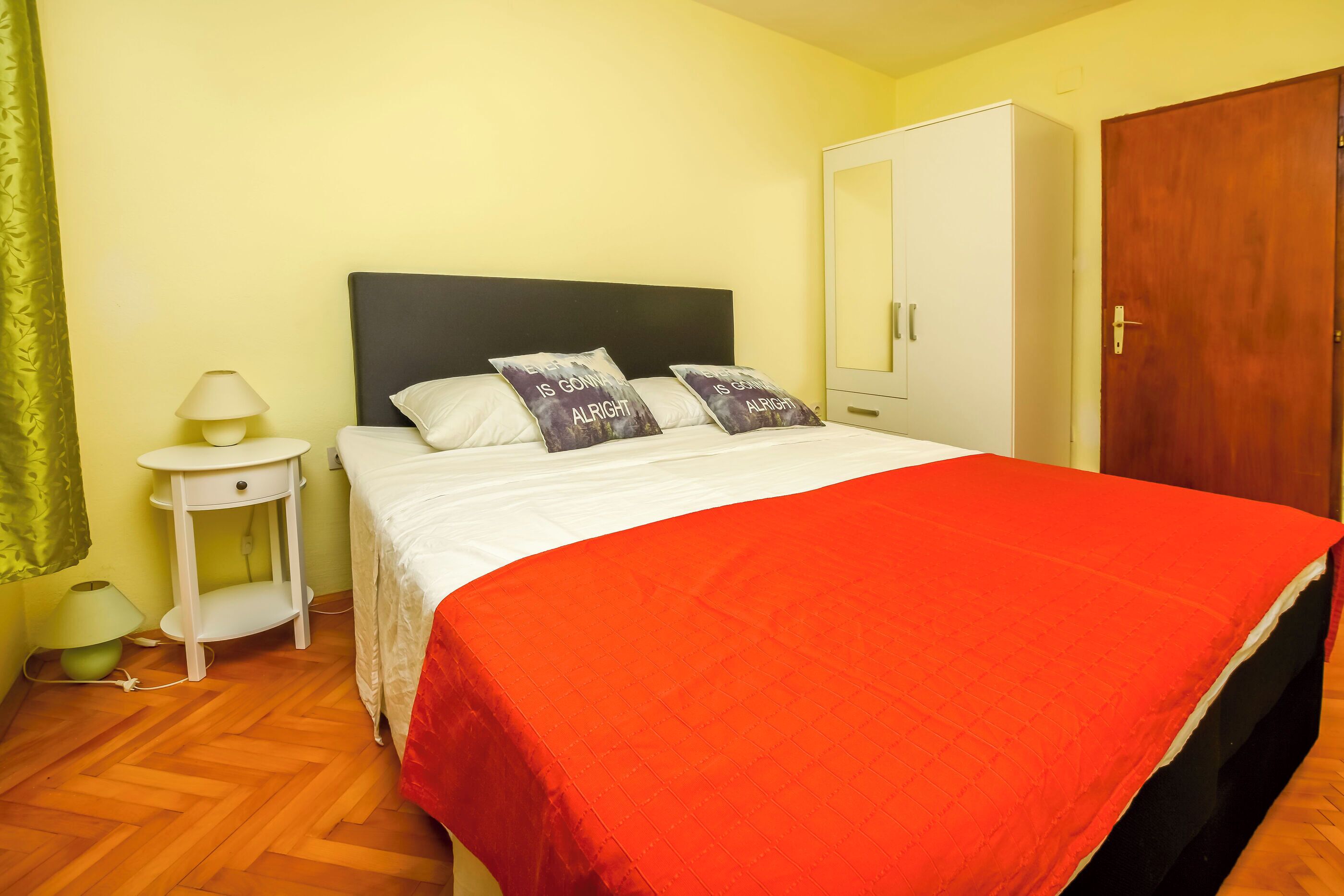 A bed with a red blanket, two pillows with text, a bedside lamp, and a wardrobe.