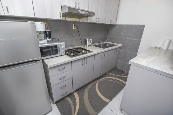 A modern kitchen with grey cabinets, a built-in microwave, a gas stove, and a sink. - Apartments Ercegovic (Rogoznica)