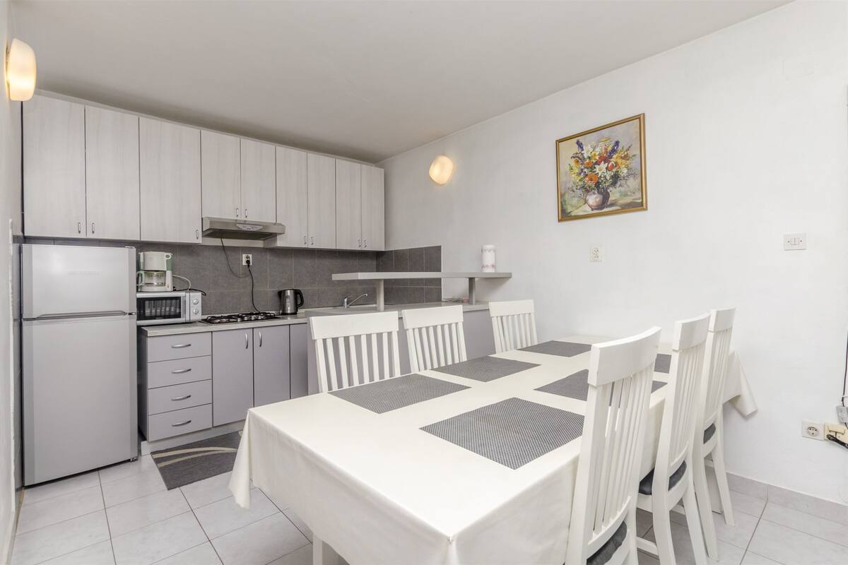 A modern kitchen with white cabinets, a dining table with chairs, and a painting on the wall.