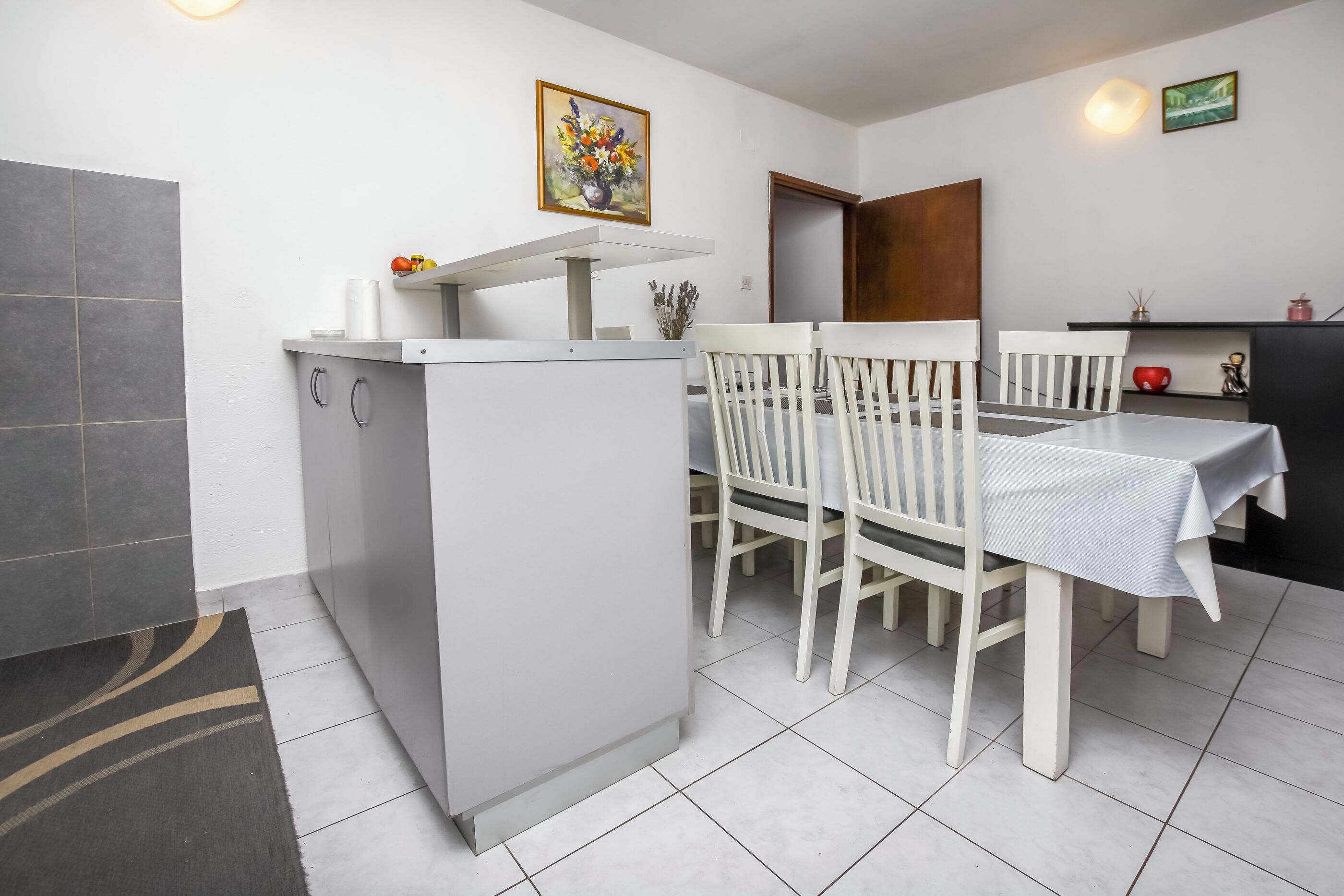Une cuisine de taille réduite, équipée d’un réfrigérateur, de meubles blancs et d’une table à manger avec des chaises.