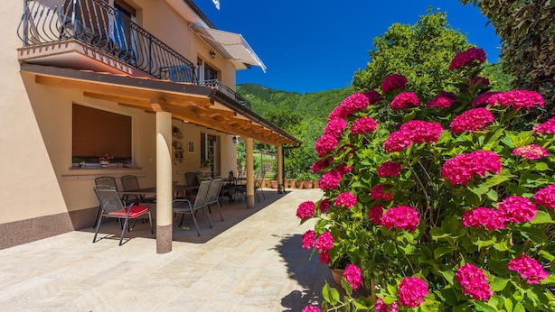 Ein zweistöckiges Gebäude mit Balkon, Sitzgelegenheit im Freien und einem Garten mit rosa Blumen.