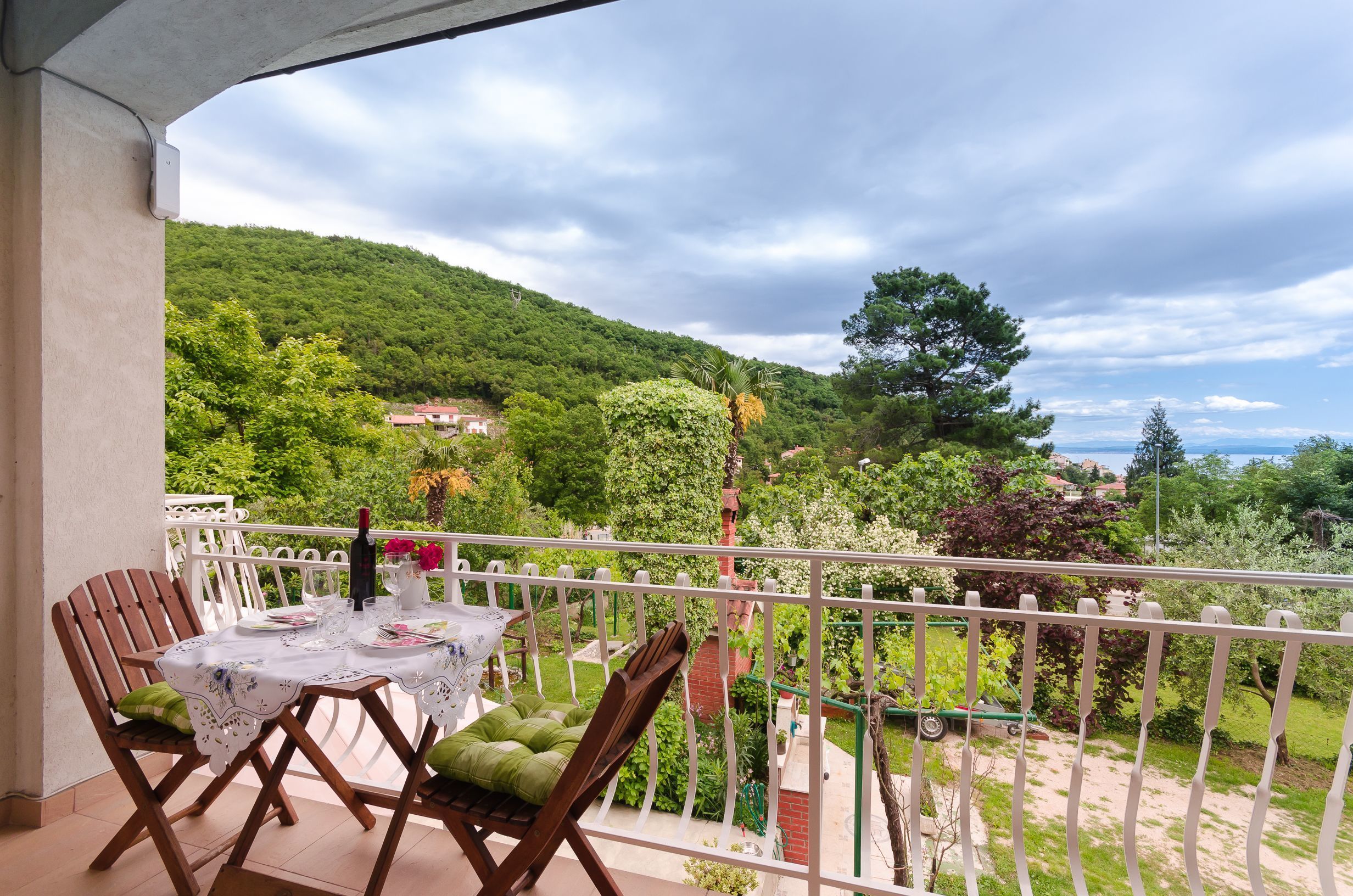 Un balcón con una mesa dispuesta para dos, con vistas a un paisaje verde exuberante y una lejana hilera de casas.