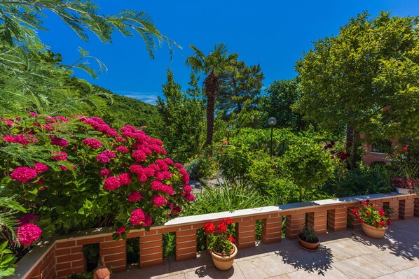 Un jardín con un banco de ladrillo, plantas en macetas y varios árboles.