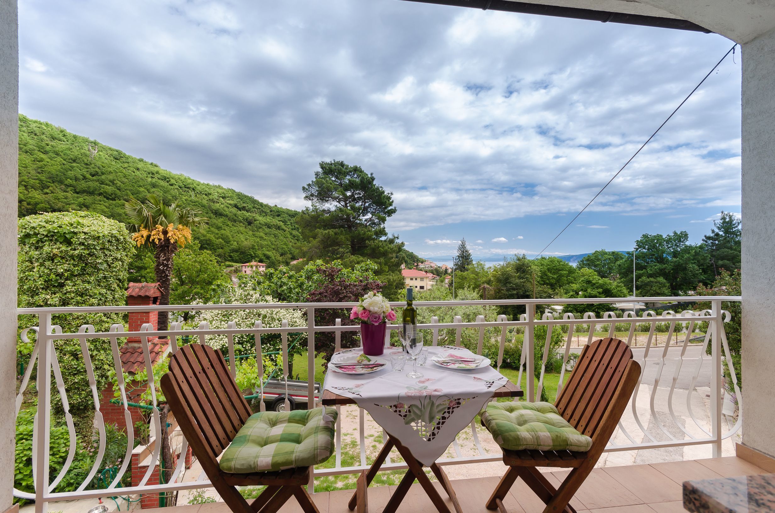 A balcony with two wooden chairs and a table set for two, overlooking a lush green landscape.